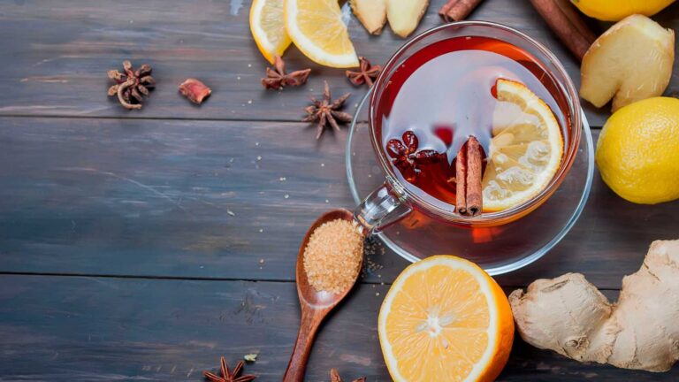 ginger tea in a glass cup, cinnamon stickes, lemon slice, spoonful of sugar