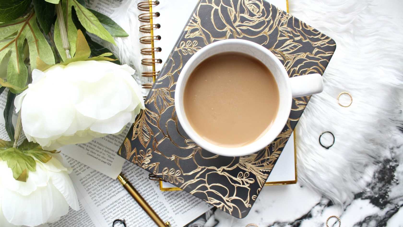 two white roses, a journal and a pen with a cup of ceylon tea with milk by side
