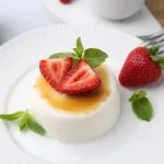 Tasty panna cotta with caramel, strawberries, mint and ceylon tea on table